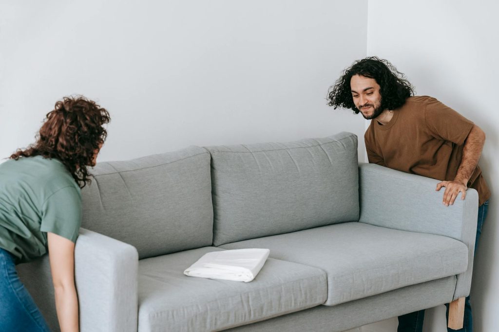 A light gray modern sofa with a white book or tablet resting on the seat cushion. The edge of a person with dark curly hair is partially visible behind the sofa's right side.