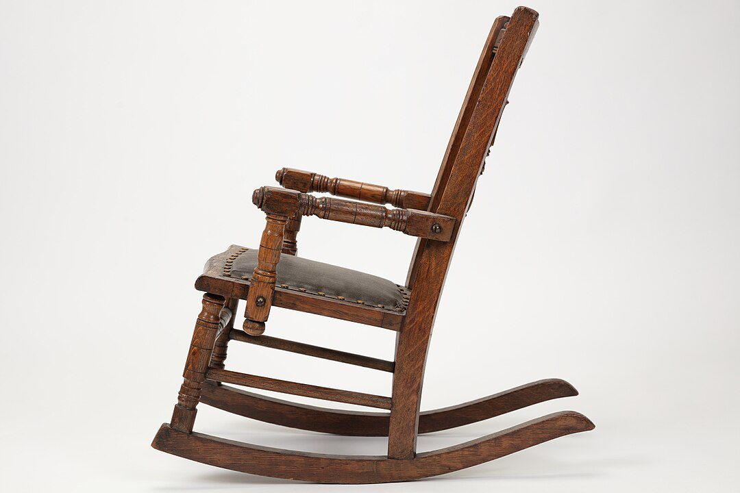 Wooden rocking chair, side view, brown polished frame, cushioned seat, curved rockers, white background