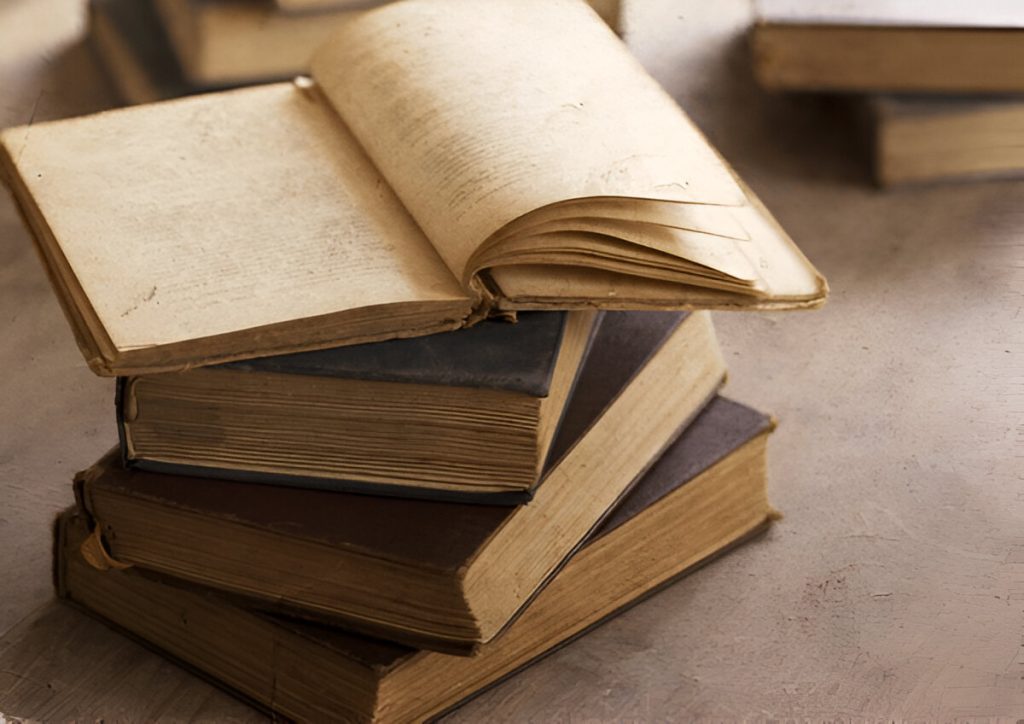 Pile of old textbooks, Stack of old books with one open on top, showing aged and yellowed pages