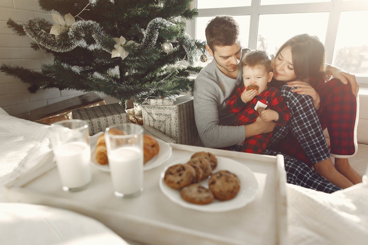 Family in matching holiday pajamas enjoying a cozy morning by the Christmas tree, with plates of cookies, croissants