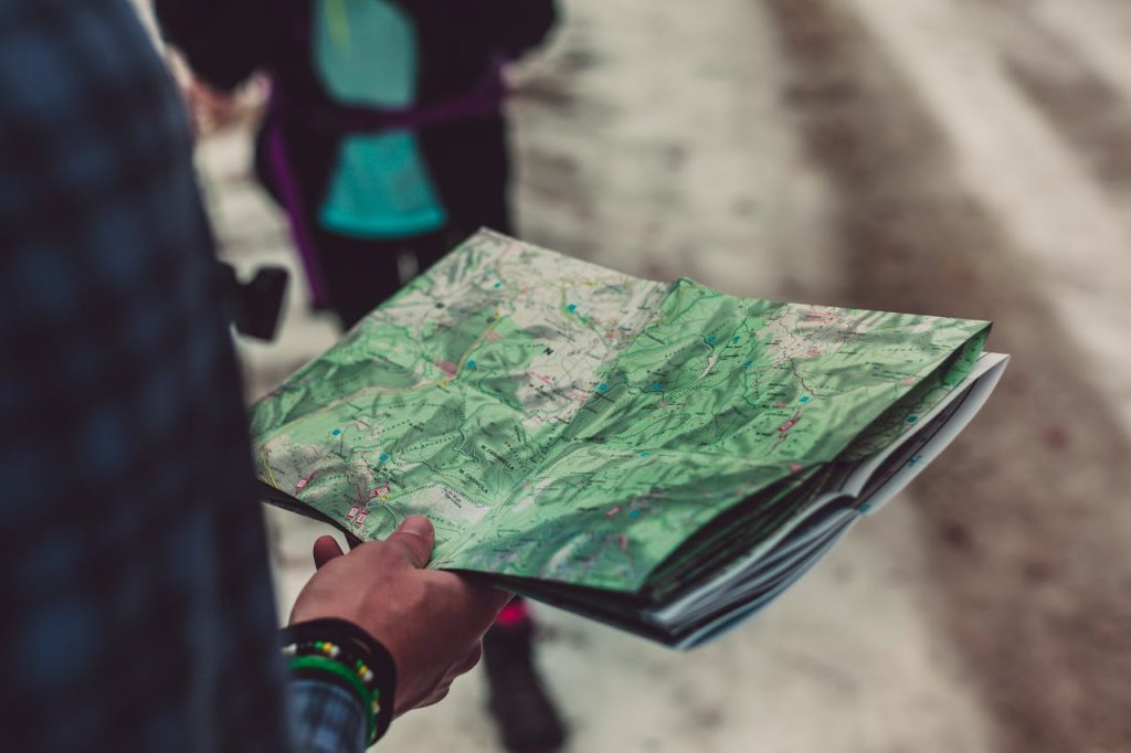 paper map, Person holding an unfolded topographic map outdoors while walking on a trail