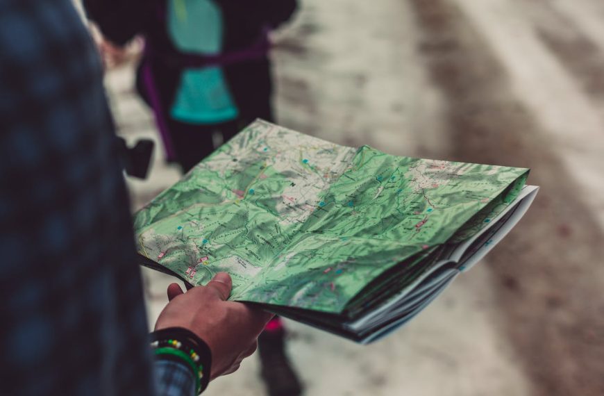 paper map, Person holding an unfolded topographic map outdoors while walking on a trail