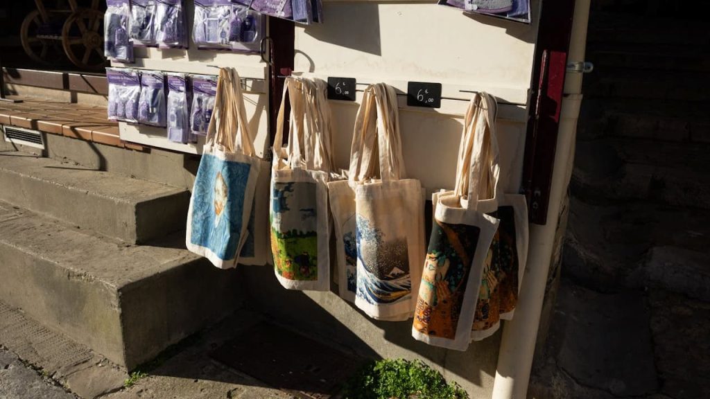 Tote bags hanging on a display rack, various colors and designs, eco-friendly, reusable, made of fabric, displayed outdoors in sunlight