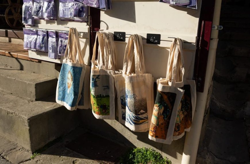 Tote bags hanging on a display rack, various colors and designs, eco-friendly, reusable, made of fabric, displayed outdoors in sunlight
