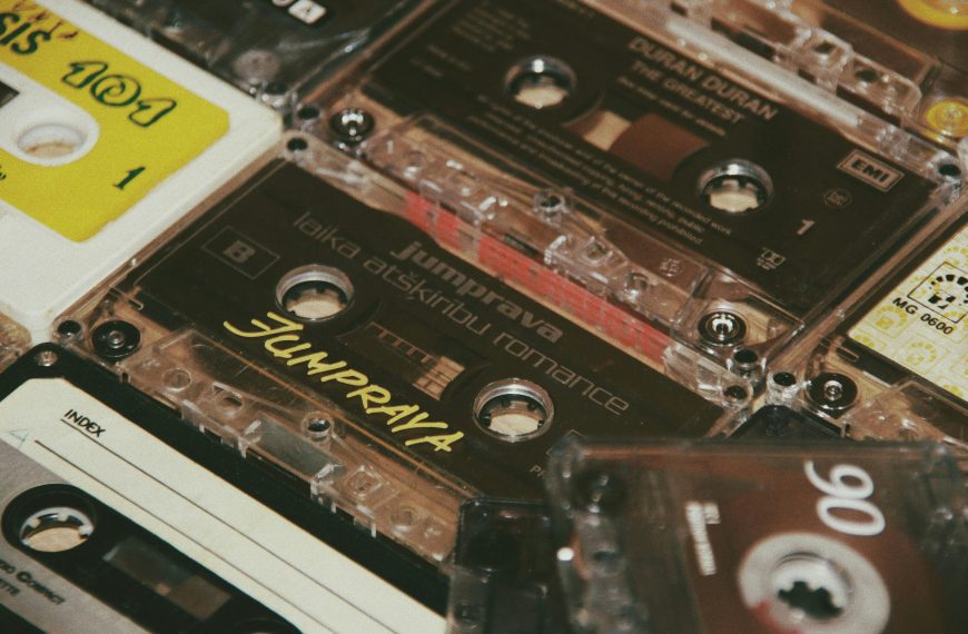 Close-up of a collection of vintage audio cassette tapes, various brands and labels visible including Jumpprava and Duran Duran, stacked in a scattered arrangement, mix of clear, white, and colored plastic casings, retro music theme emphasized by nostalgic design elements