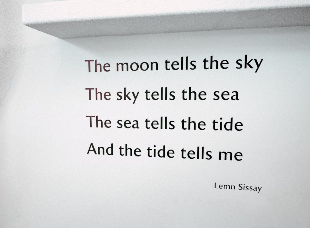 Poem text on a white wall under a ledge, reading “The moon tells the sky, The sky tells the sea, The sea tells the tide, And the tide tells me” by Lemn Sissay