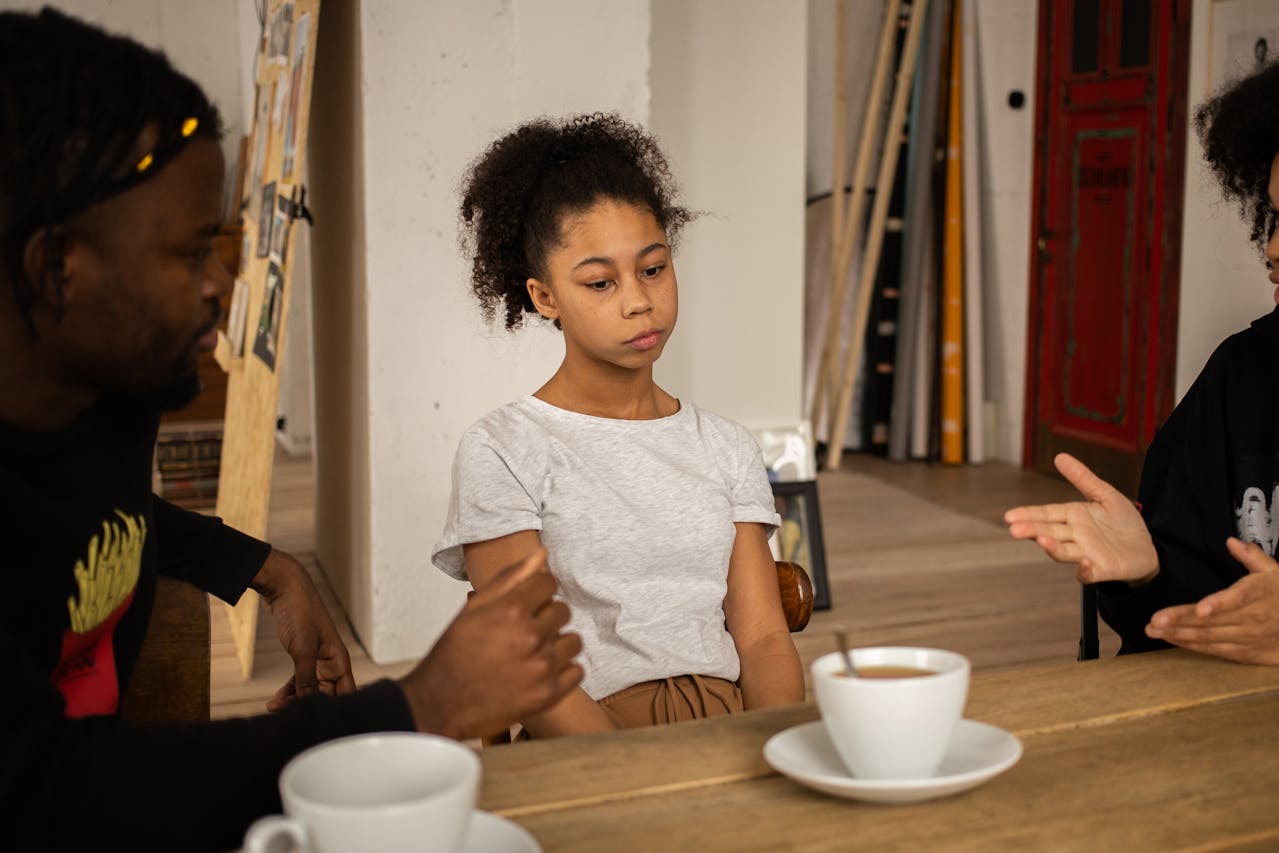 Young girl sits quietly between two adults having a serious conversation at a table with coffee cups