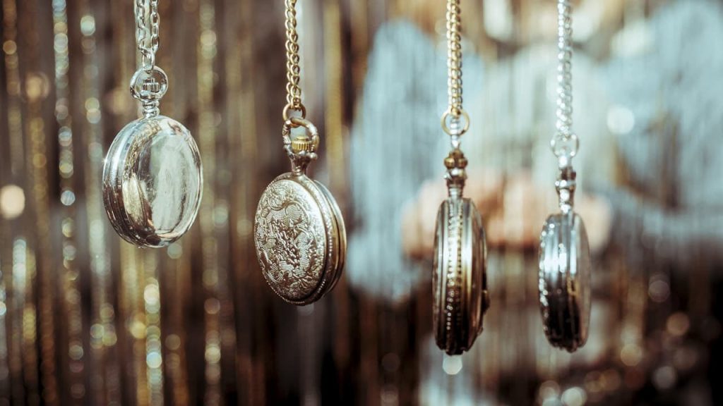 Pocket watches hanging on chains, vintage style, blurred golden background, person holding watches, antique and classic designs, metallic finishes reflecting light