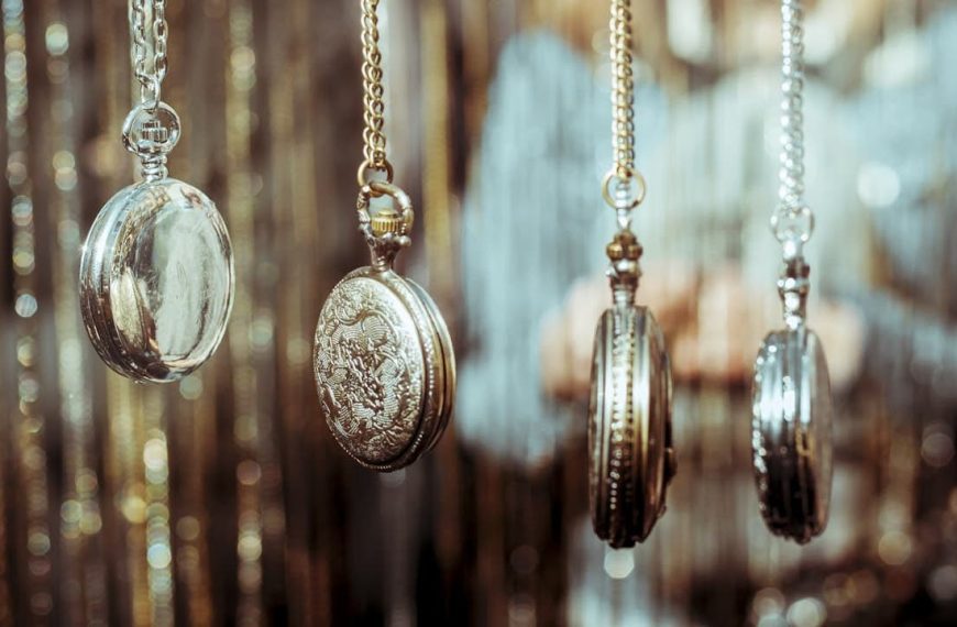 Pocket watches hanging on chains, vintage style, blurred golden background, person holding watches, antique and classic designs, metallic finishes reflecting light