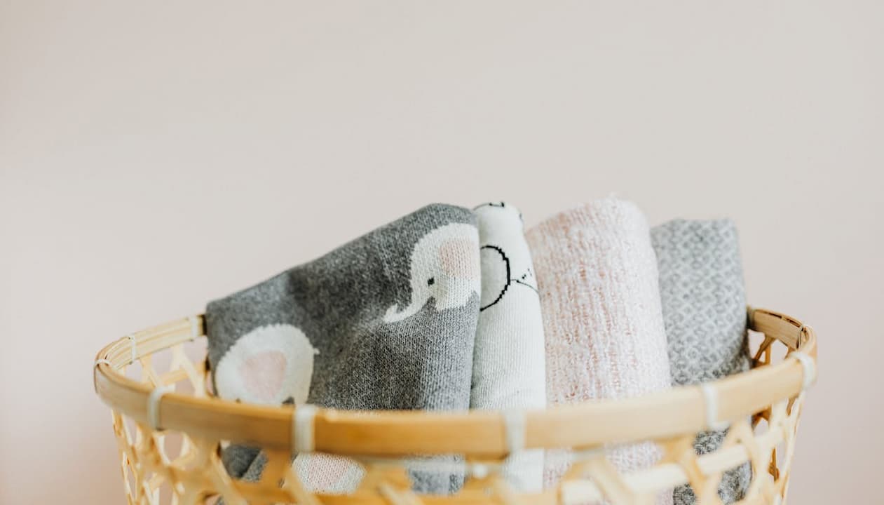 Wicker basket, rolled towels, grey and white colors, soft fabric texture, neutral background, minimalistic bathroom or spa decor, clean and organized arrangement