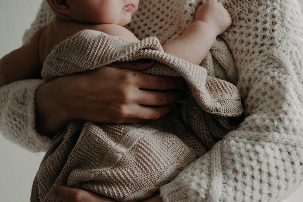 Close-up of a baby wrapped in a knitted blanket, held gently by an adult hand