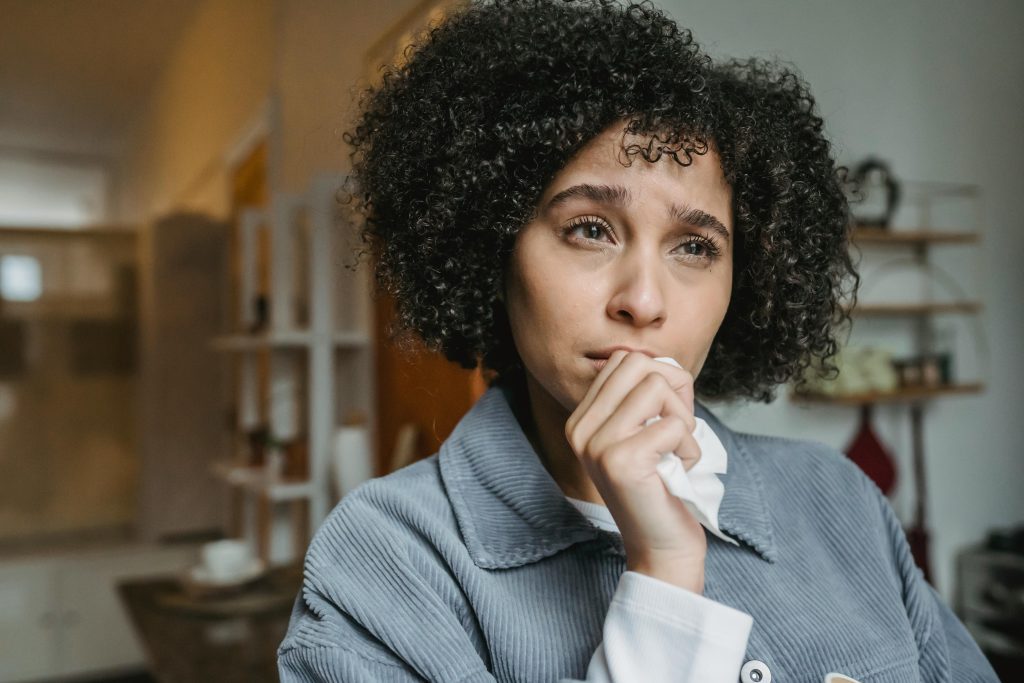 A woman with curly hair holding a tissue looks emotional and teary-eyed indoors