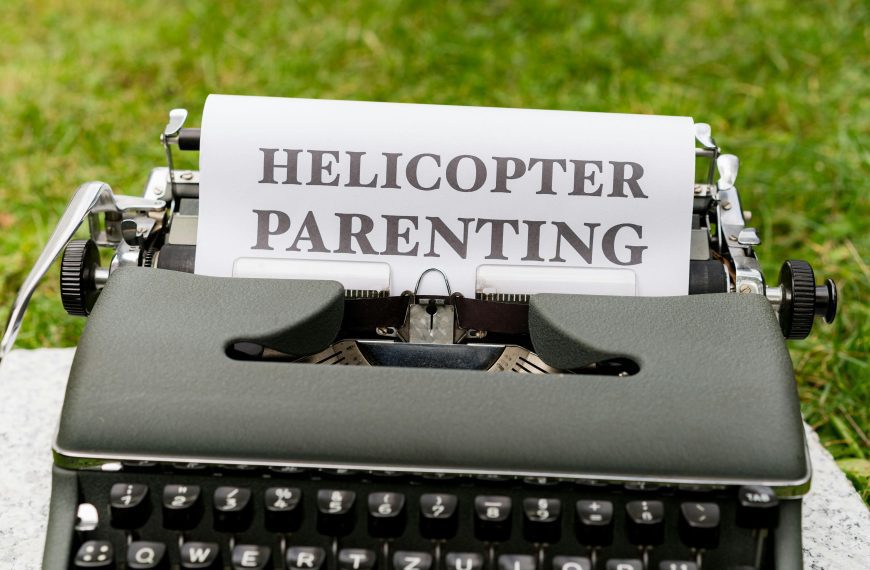 A typewriter with a sheet of paper displaying the bold words “HELICOPTER PARENTING,” set outdoors on green grass
