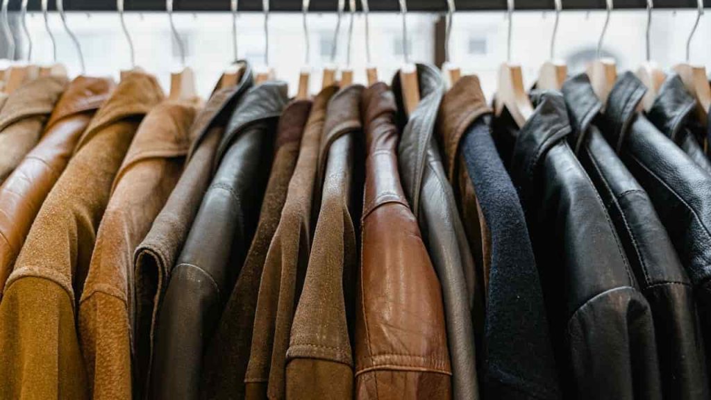 Row of assorted leather and suede jackets, brown and black shades, hanging on wooden hangers, on a metal clothing rack