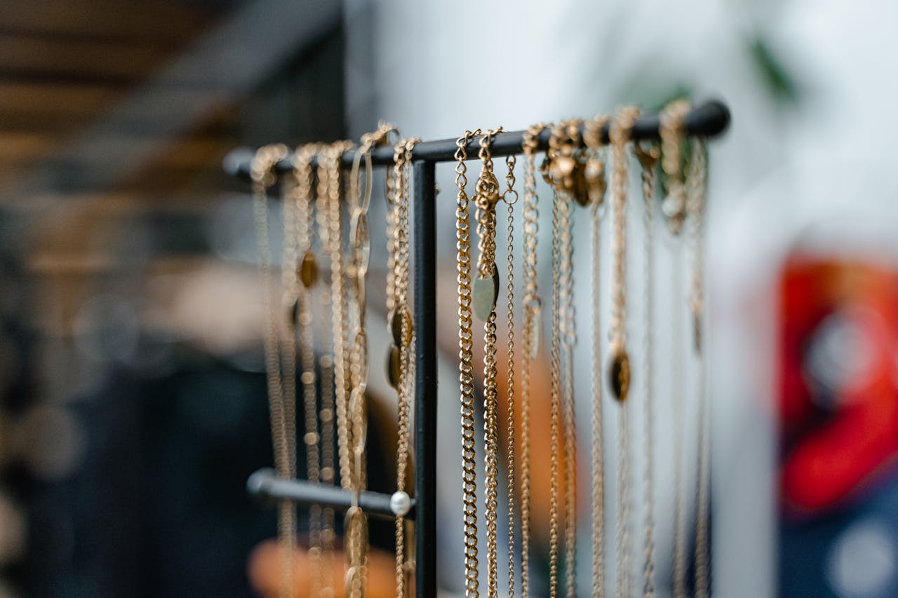 Close-up of gold necklaces hanging on a black metal jewelry rack, various chain styles and pendants, blurred indoor background with soft lighting