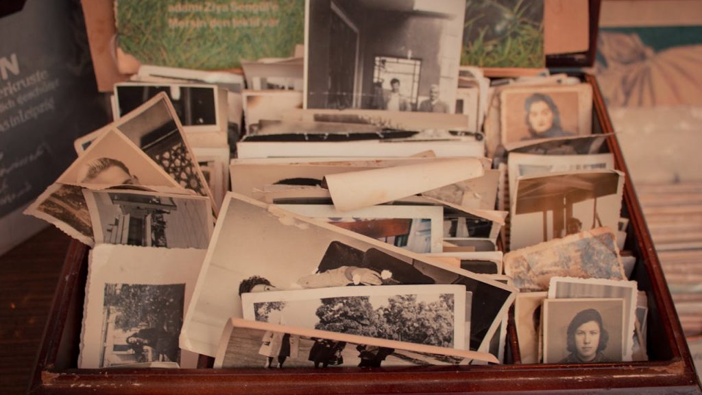 Box filled with old black-and-white and sepia-toned photographs, showing various people and scenes, some photos curled or worn