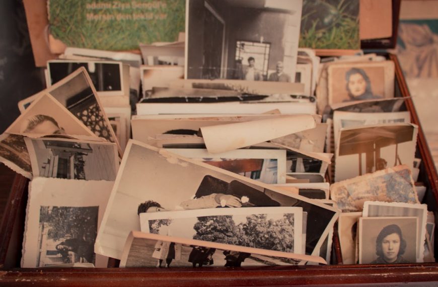 Box filled with old black-and-white and sepia-toned photographs, showing various people and scenes, some photos curled or worn