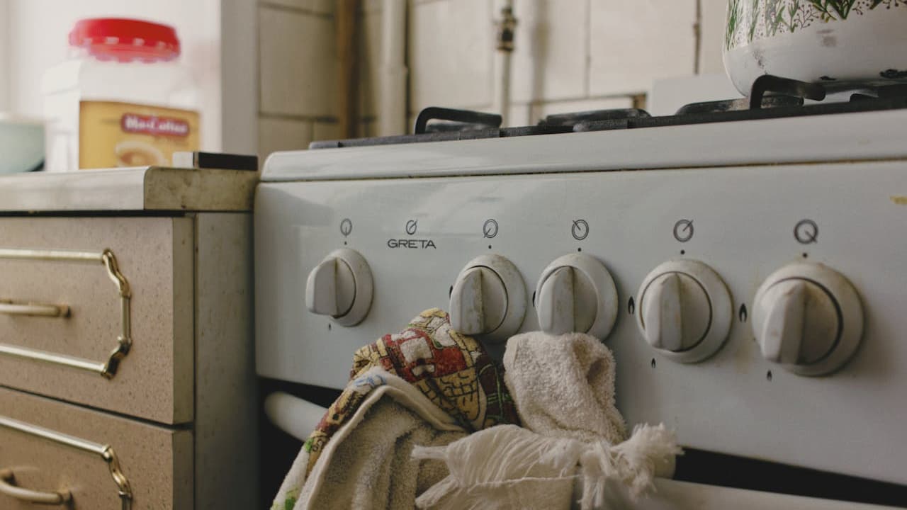 Vintage kitchen stove with metallic control knobs, dish towels hanging on the oven handle, retro-style countertop with food containers, warm lighting, nostalgic kitchen setting