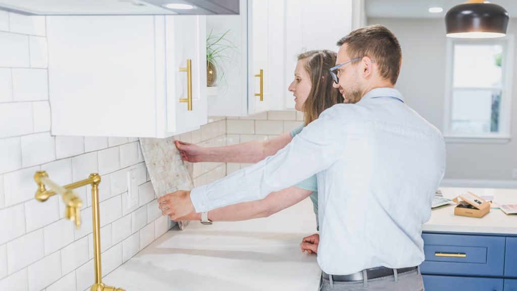 Couple holding a tile sample against a kitchen wall while discussing backsplash options
