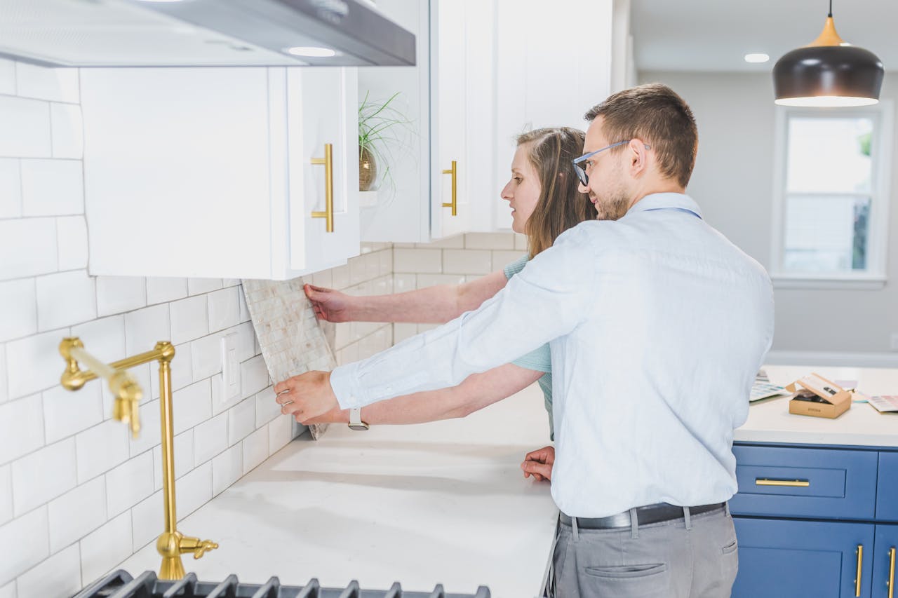 Couple holding a tile sample against a kitchen wall while discussing backsplash options