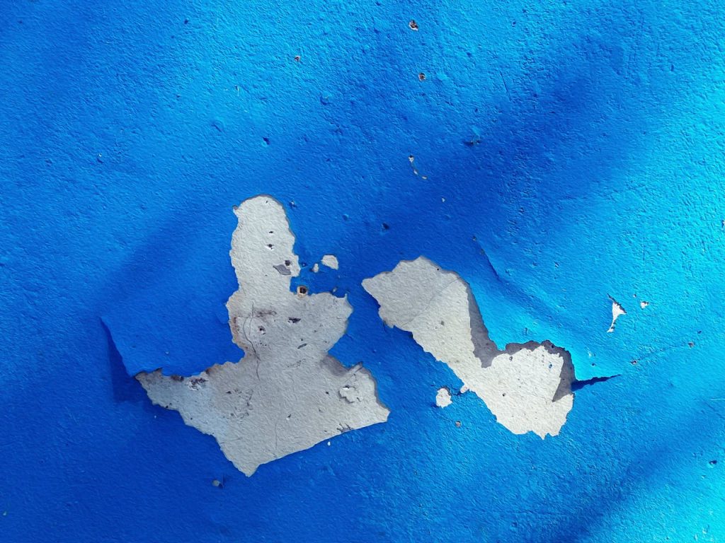 Blue painted wall with peeling paint revealing a light gray underlayer, two large chipped sections in the center