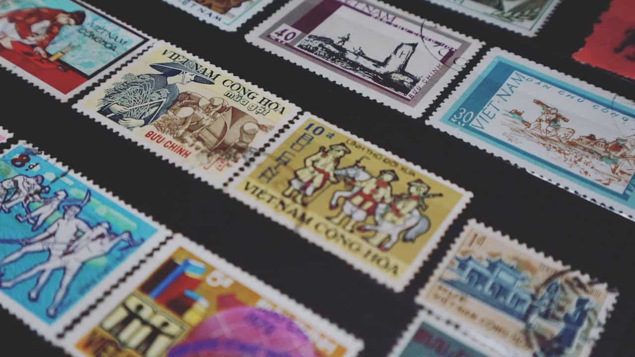 Assorted vintage Vietnamese postage stamps, arranged on a black display background, featuring illustrations of soldiers, cultural scenes, historic landmarks, and traditional clothing, with varied colors including blue, yellow, red, and white
