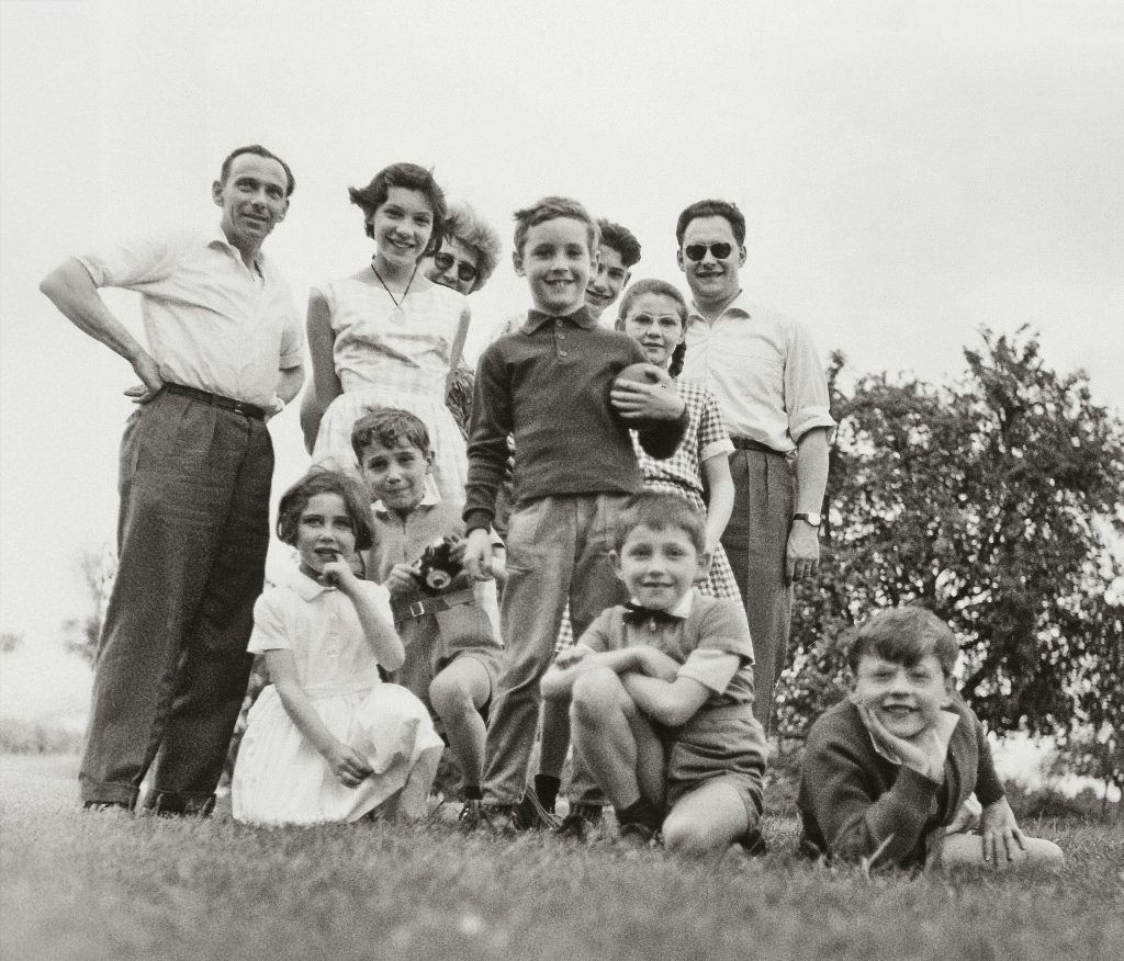 Black and white photo of a large family group posing outdoors, smiling adults and children, taken from a low angle on grass