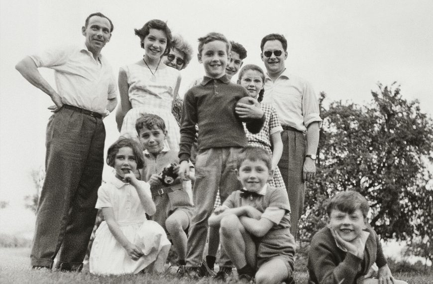 Black and white photo of a large family group posing outdoors, smiling adults and children, taken from a low angle on grass