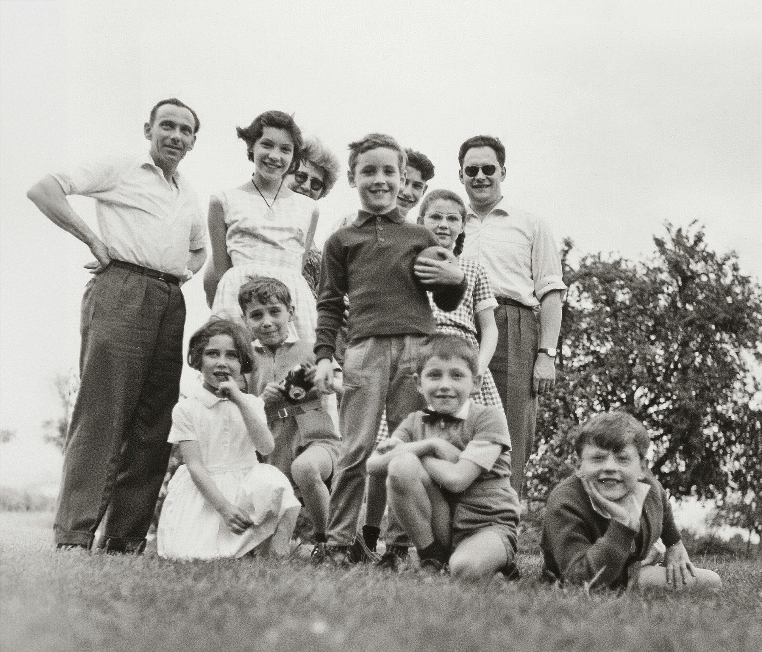 Black and white photo of a large family group posing outdoors, smiling adults and children, taken from a low angle on grass