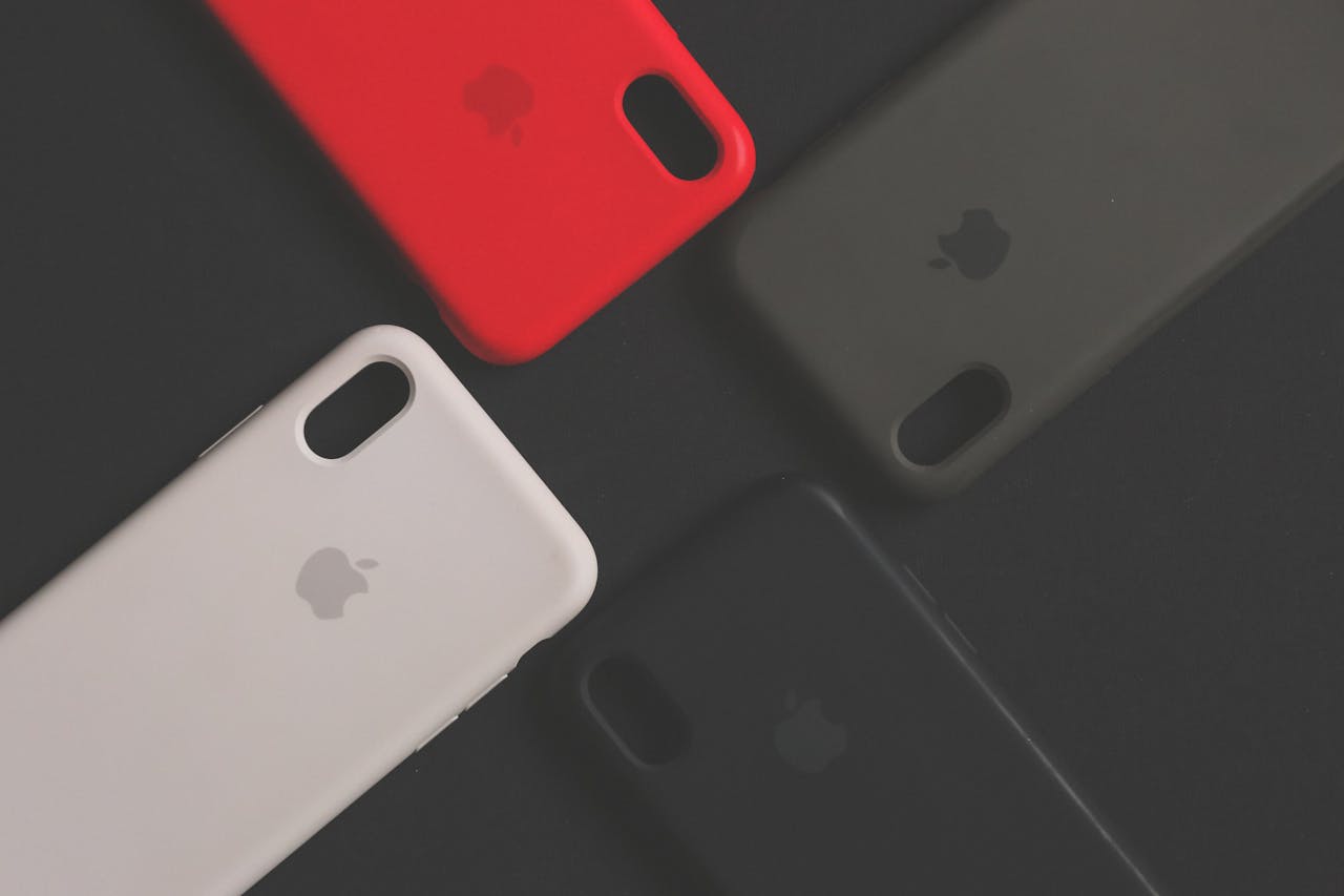 Four Apple iPhone cases in red, black, gray, and white on a dark background