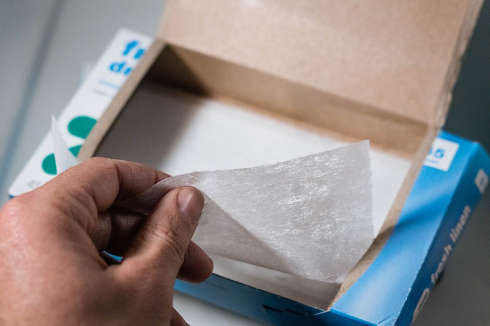 Hand pulling out a white dryer sheet from an open box, cardboard packaging visible in background