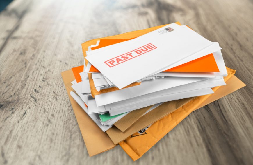 Stack of envelopes and mail on a wooden surface, with one envelope marked “PAST DUE” in red text