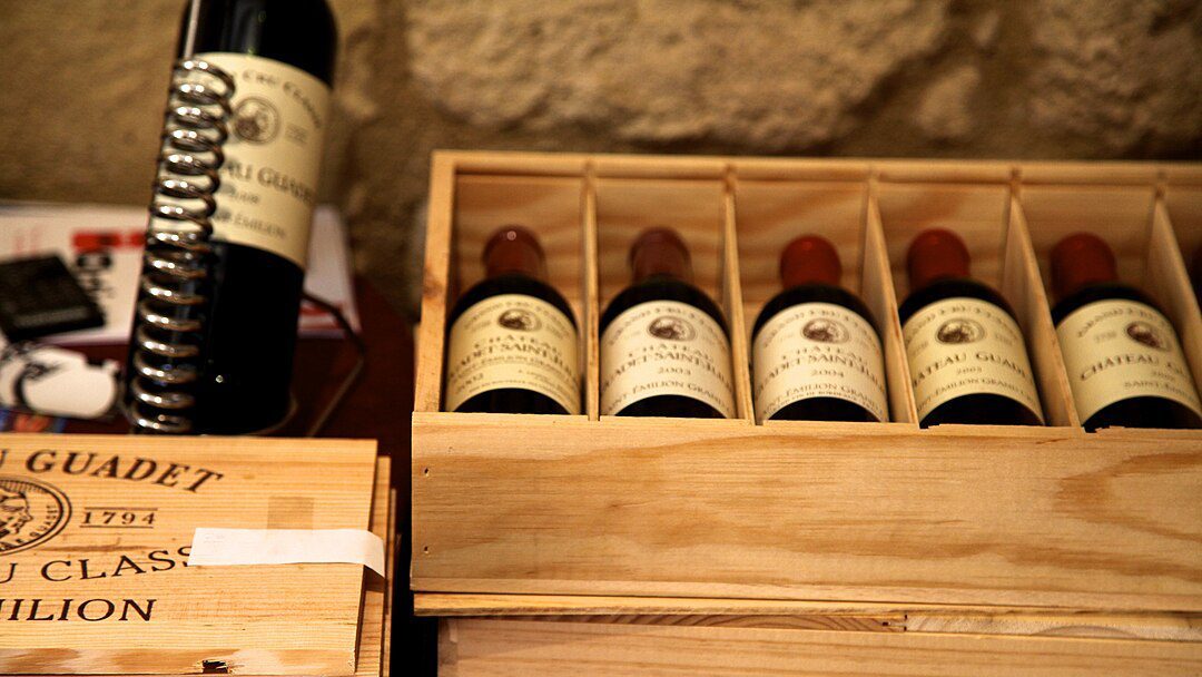 wooden wine crate, five wine bottles with cream labels, vintage-style packaging, wine storage box, stacked wine bottles, winery branding visible, rustic wooden case, display of collectible wines, premium wine selection, gift or export packaging