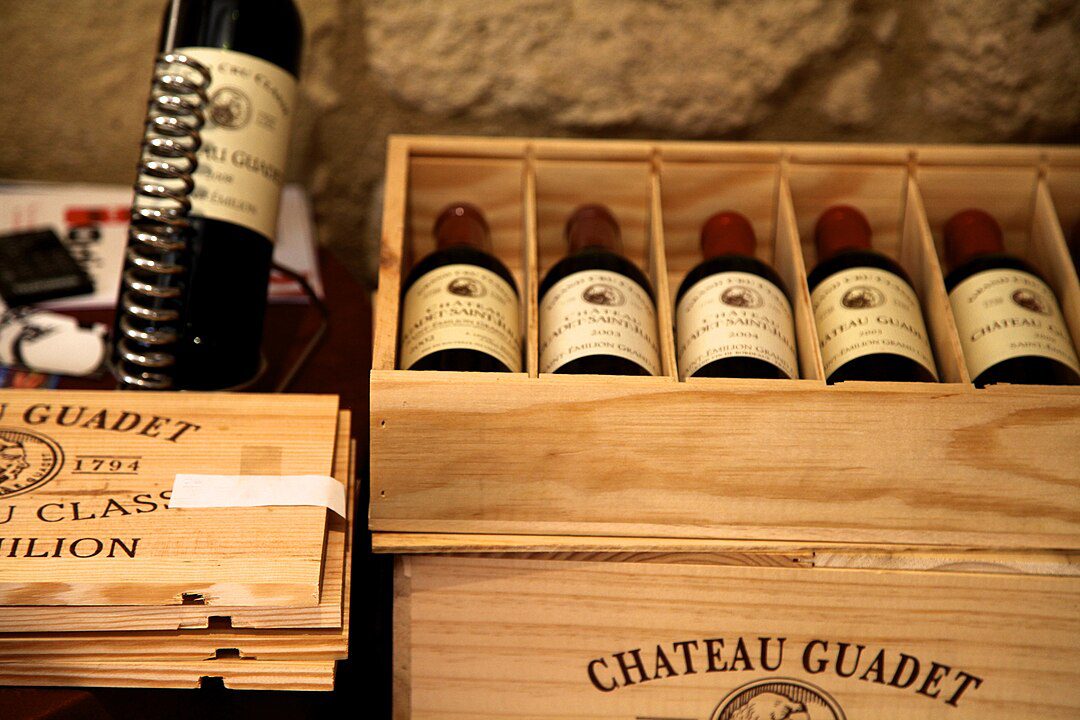 wooden wine crate, five wine bottles with cream labels, vintage-style packaging, wine storage box, stacked wine bottles, winery branding visible, rustic wooden case, display of collectible wines, premium wine selection, gift or export packaging