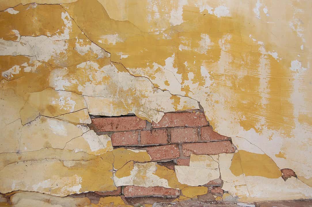 cracked wall, visible horizontal and vertical cracks, chipped paint, exposed plaster, uneven surface, signs of structural stress