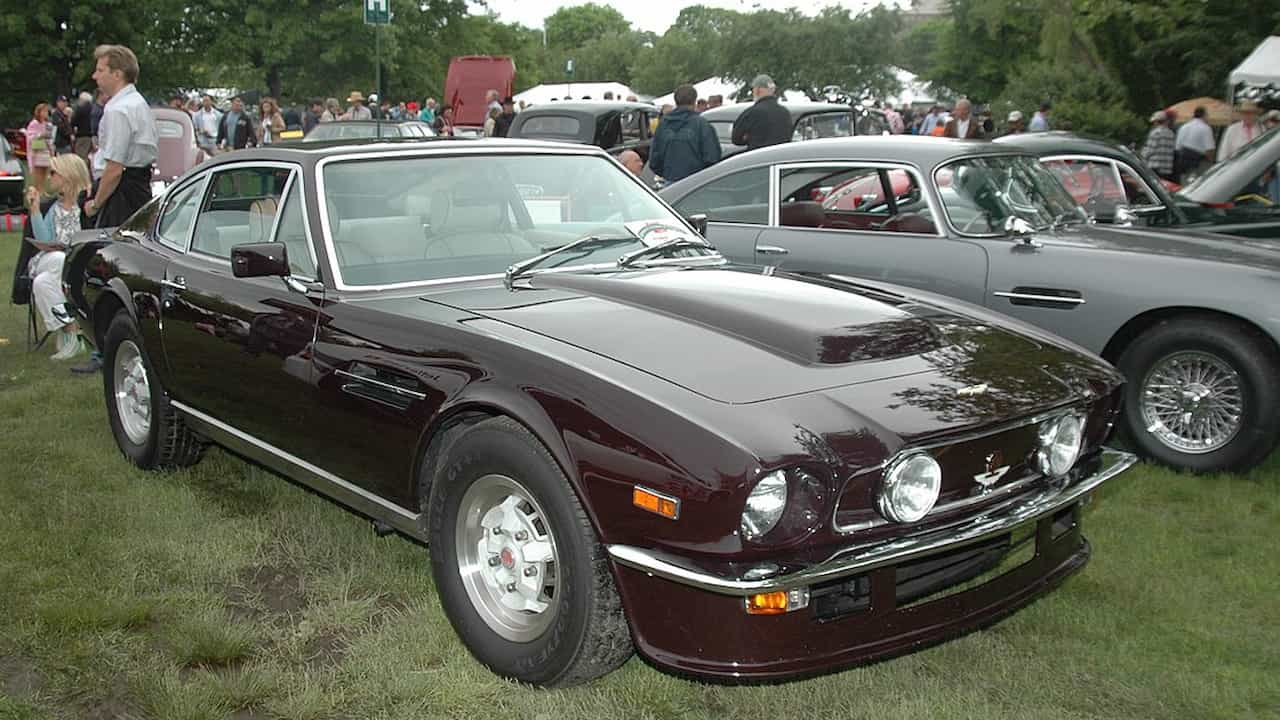 1977 Aston Martin V8 Vantage, classic British grand tourer, dark green exterior, long hood, mesh front grille, quad headlights, hood bulge, chrome trim, elegant fastback styling, alloy wheels