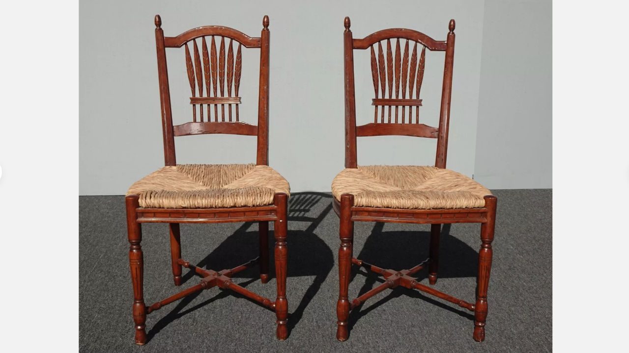 pair of vintage 1960s wooden rush chairs with carved spindle backs, woven straw seats, and turned legs, placed on grey carpet with plain wall background