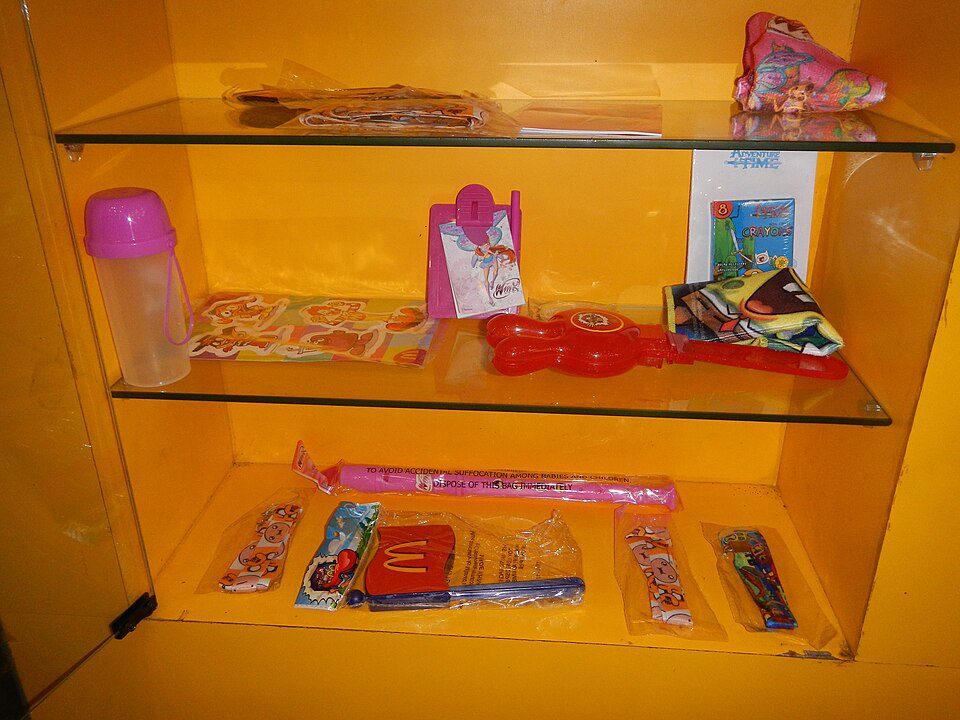 Glass display case, bright yellow background, filled with assorted candy and snacks, pink water bottle on the left, candy sticks and packets arranged on three shelves, colorful packaging, nostalgic treat selection