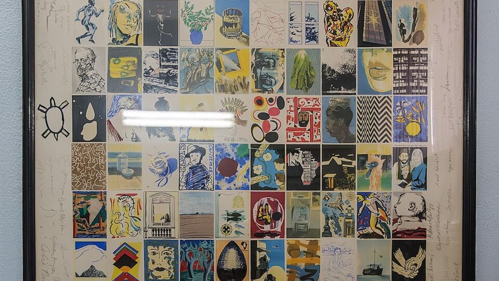 Framed collection of signed band posters, arranged in a grid layout, showcasing various bands, album art, and autographs, behind reflective glass