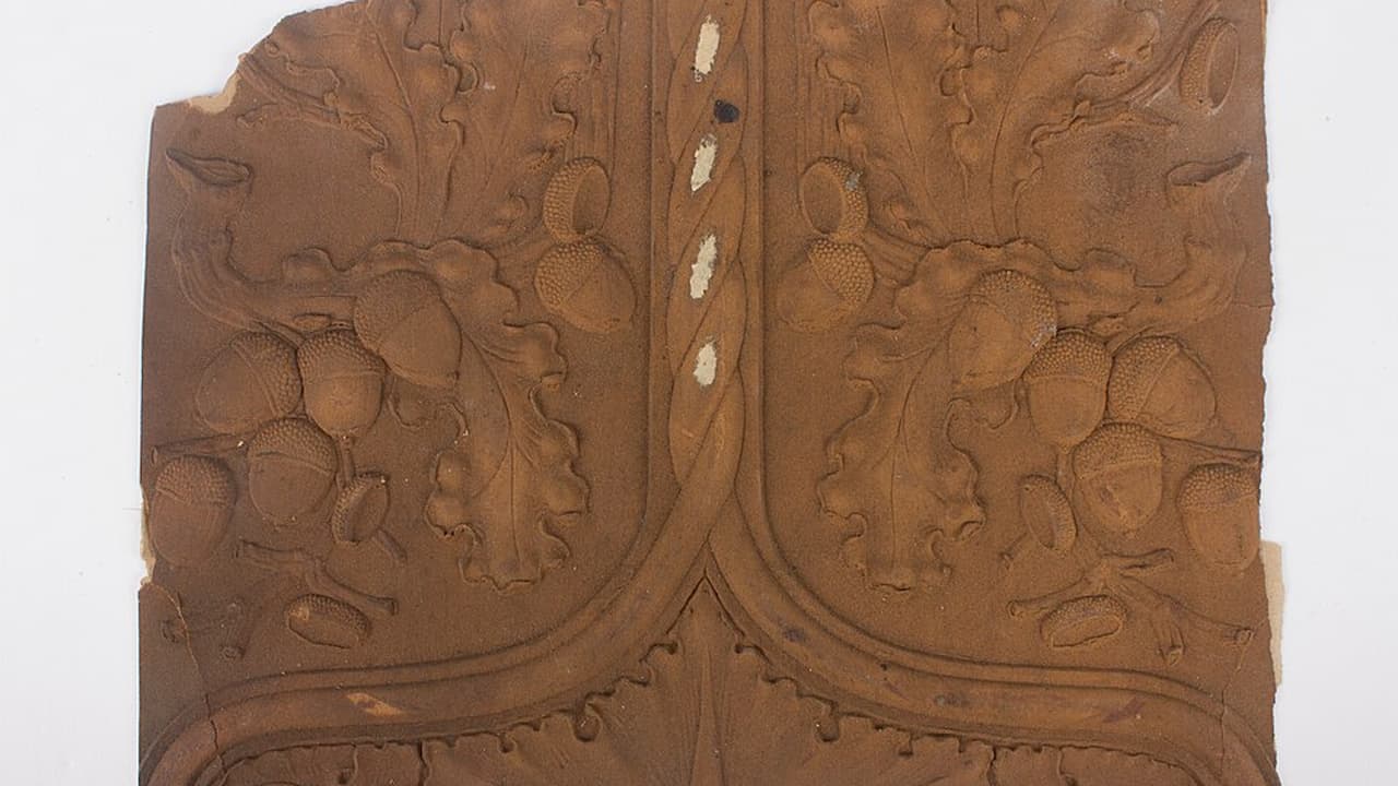 Aged wallpaper scrap, brown with intricate symmetrical floral and vine patterns, slightly torn edges, visible vertical seam, vintage or antique design