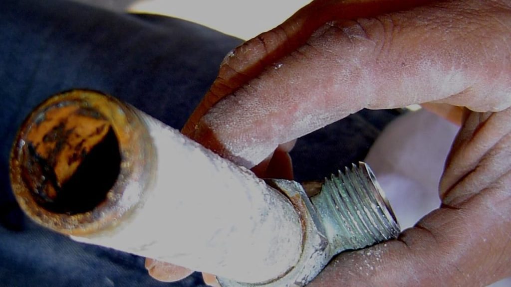 galvanized plumbing pipe, rusted surface, flaking metal, reddish-brown corrosion, threaded joints worn, signs of leakage, aged appearance