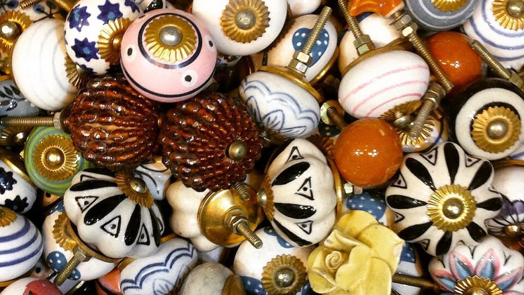 Colorful assortment of decorative drawer knobs, ceramic and metal finishes, various patterns and textures, tightly grouped display, vintage and handmade appearance, mix of floral, striped, and geometric designs