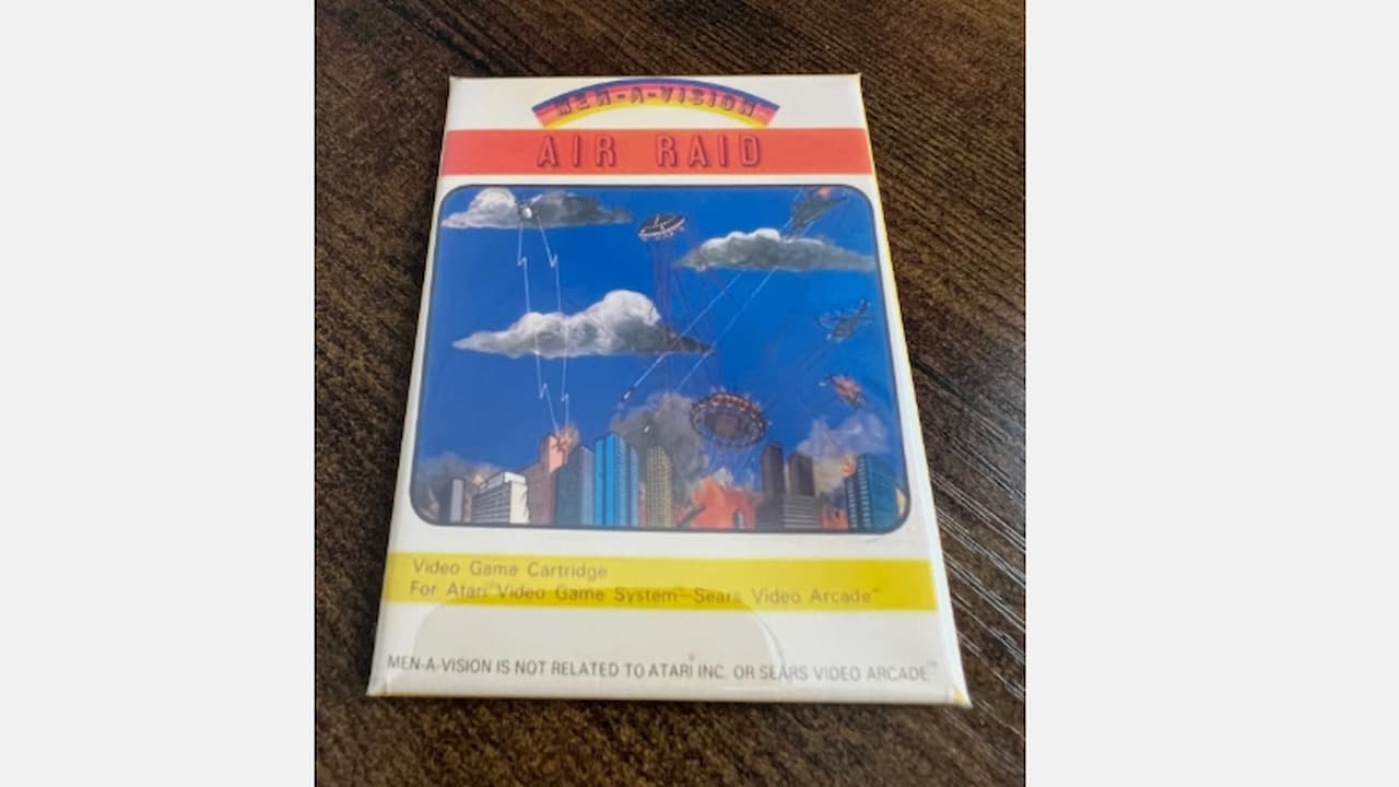 Air Raid video game box, Men-A-Vision branding, illustrated city skyline under attack, UFOs in the sky, clouds with lightning bolts, vintage packaging for Atari video game cartridge