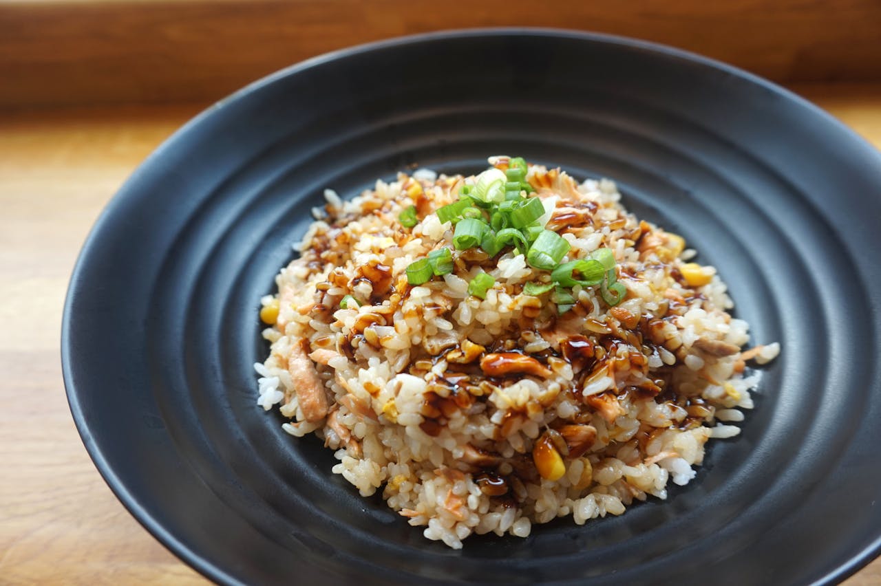 Bowl of baked brown rice, topped with chopped spring onions and dark soy-based sauce, served on a black plate