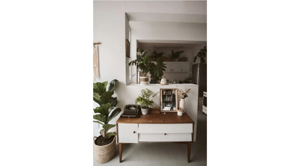 Indoor space with a mid-century wooden console, surrounded by large and small potted fake plants