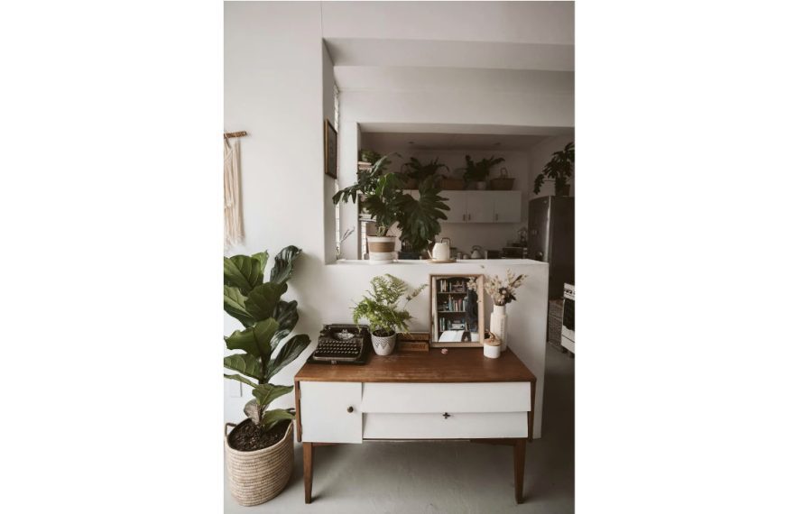 Indoor space with a mid-century wooden console, surrounded by large and small potted fake plants