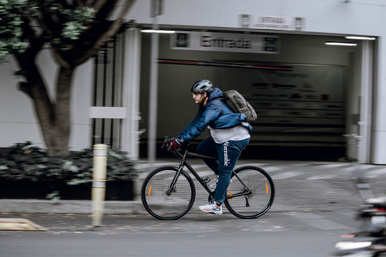 Man riding a black bicycle on the street, wearing a helmet, blue jacket, and backpack