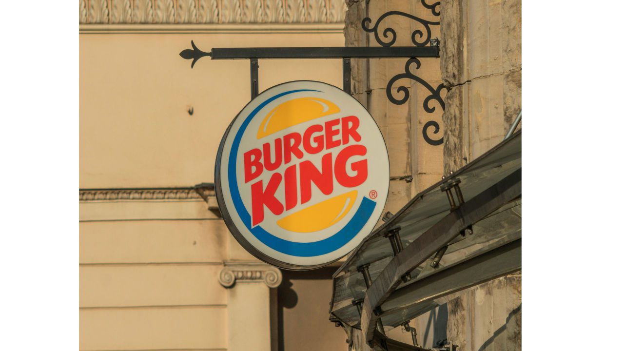 Burger King logo sign, circular design, red text, yellow bun graphic, blue outline, mounted on ornate black bracket