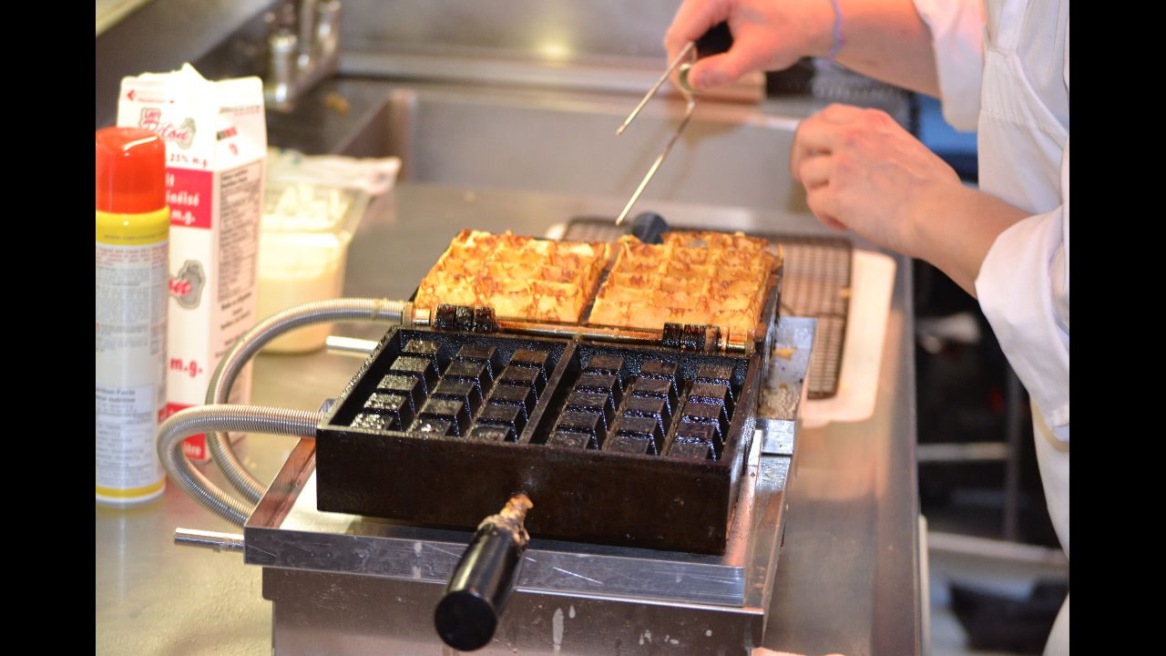 Cast iron waffle iron cooking golden brown waffles on stovetop with person using tongs in commercial kitchen