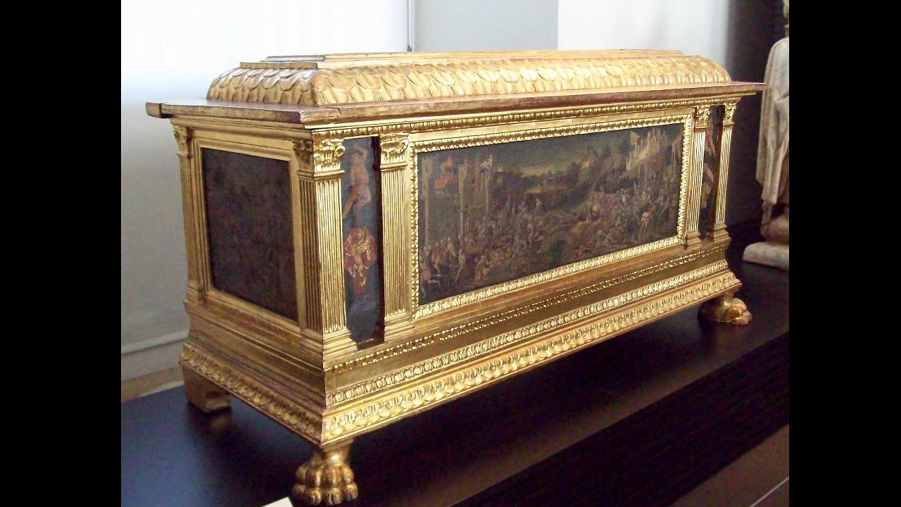 Ornate antique cedar hope chest with gold trim, decorative paintings, and claw feet, displayed on a dark surface